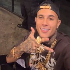 a man with tattoos and gold jewelry giving the thumbs up sign in front of him