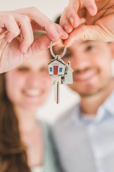 a man and woman holding up a house shaped keychain to their new home