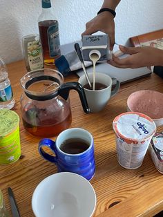 a table with cups and saucers on top of it, one person is pouring something into the other