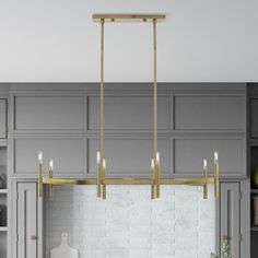 a kitchen with gray cabinets and white counter tops, gold chandelier over the island