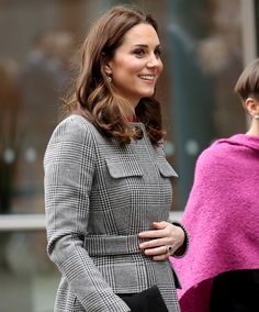 the pregnant woman is wearing a coat and holding her hand on her hip as she walks down the street