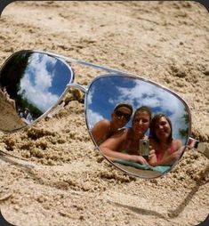 two people are taking a selfie in the reflection of sunglasses on the sandy beach