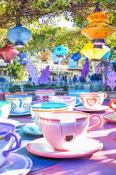 colorful tea cups and saucers are lined up on a table with paper lanterns in the background