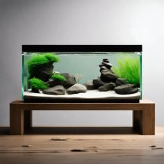 an aquarium with rocks and plants in it on a wooden table next to a gray wall