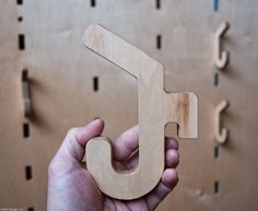 a hand holding a wooden object in front of a wall with letters on it and hooks