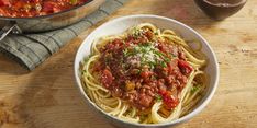 a bowl of spaghetti with meat and tomato sauce next to a glass of red wine