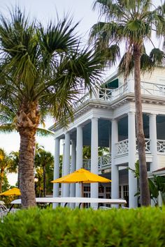 a large white house with palm trees and yellow umbrellas