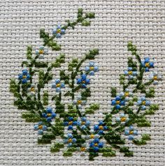 blue and yellow flowers are embroidered onto the side of a piece of white fabric with green leaves