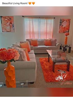 a living room filled with furniture and orange flowers on top of a table in front of a window