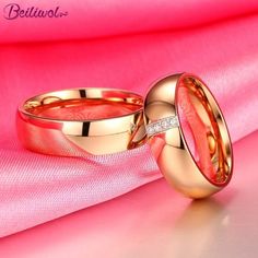 two gold wedding rings sitting on top of a pink satin material background with diamonds in the middle