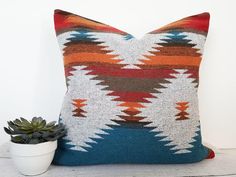 a colorful pillow sitting on top of a wooden table next to a potted plant