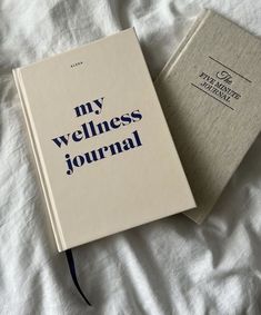 an open book sitting on top of a bed next to a closed book with the words my wellness journal