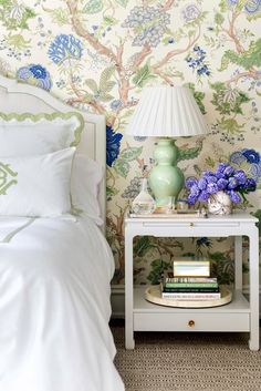 a white bed sitting next to a nightstand with blue flowers on it