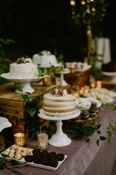 a table topped with cakes and desserts on top of a wooden table covered in greenery