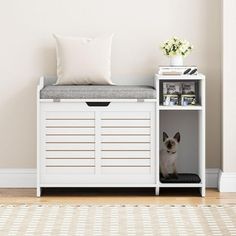 a small dog sitting in a white storage unit next to a pillow on top of a rug