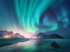 an aurora bore over the mountains and water at night with bright lights in the sky