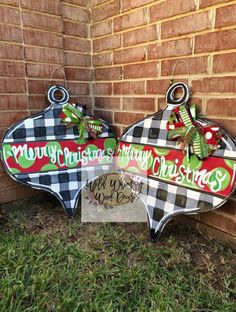 two christmas signs sitting on the grass next to a brick wall