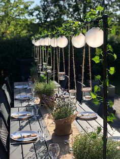 an outdoor dining table set with place settings and hanging planters on the top of it