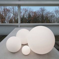 three large white balls sitting on top of a cement floor next to each other in front of a window