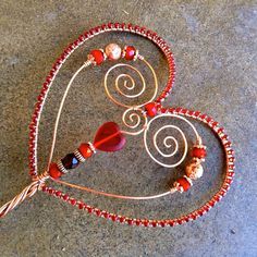 a heart shaped wire sculpture with beads and glass bead work on the sides, sitting on a concrete surface