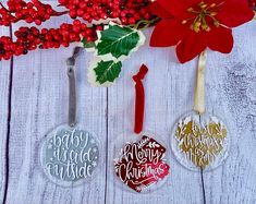 three christmas ornaments are hanging on a white wooden table with red berries and holly leaves