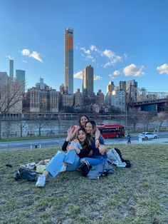 two women sitting on the grass in front of a city skyline