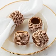 three napkin holders sitting on top of a plate next to a white napkin and gold trim