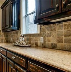 a kitchen with granite counter tops and dark wood cabinetry, along with marble tile backsplash