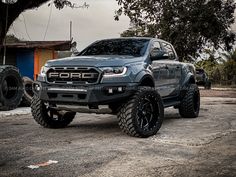 a gray truck parked on top of a dirt road next to a tree and building