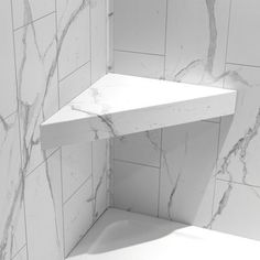 the corner of a bathroom with white marble tiles on the walls and floor, as well as a shelf