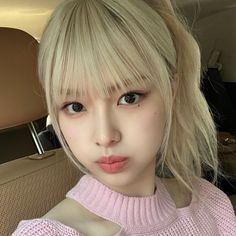 a close up of a person with blonde hair wearing a pink sweater and looking at the camera