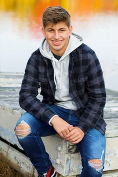 a young man sitting on top of a wooden bench next to a body of water