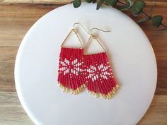 red and white beaded earrings sitting on top of a plate next to a plant