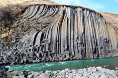 a large rock formation next to a body of water on top of a rocky hillside