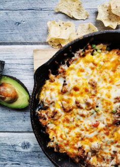 a skillet filled with mexican food and tortilla chips next to an avocado