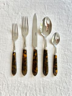 four forks, two spoons and one knife on a white tablecloth with animal print