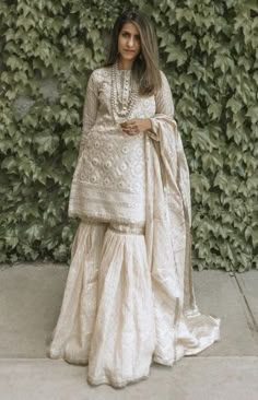 a woman standing in front of a green wall wearing a white dress and shawl