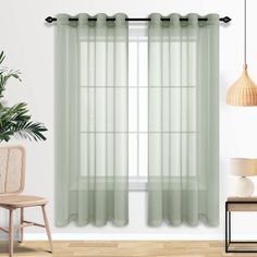 a living room with white walls and green drapes on the windowsill, a chair, and a potted plant