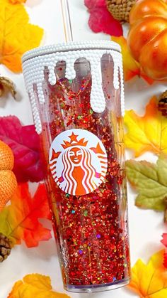 a starbucks cup with red sprinkles on it next to fall leaves and pumpkins