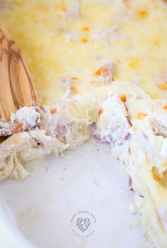 a wooden spoon in a casserole dish with meat and cheese on the side