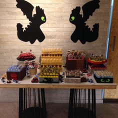 a table topped with cakes and cupcakes covered in icing next to a brick wall