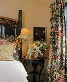 there is a bed with flowers on it next to a table and lamp in the room