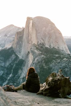 a woman sitting on top of a mountain next to a tree stump