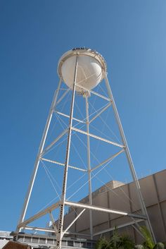 a tall white water tower sitting in front of a building with a blue sky behind it