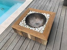 a bowl sitting on top of a wooden table next to a pool with rocks and pebbles