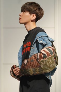 a young man wearing a denim jacket and black t - shirt carrying a large bag