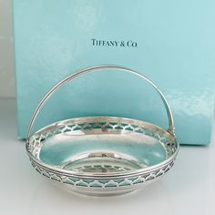 a silver basket sitting on top of a table next to a blue box with the words tiffany & co