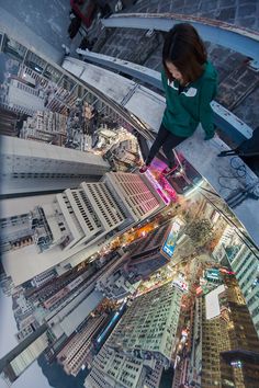 a woman standing on top of a tall building looking down at the city lights and skyscrapers