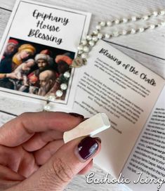 a person holding an open book on top of a wooden table next to a necklace