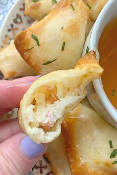 a hand holding a pastry with dipping sauce